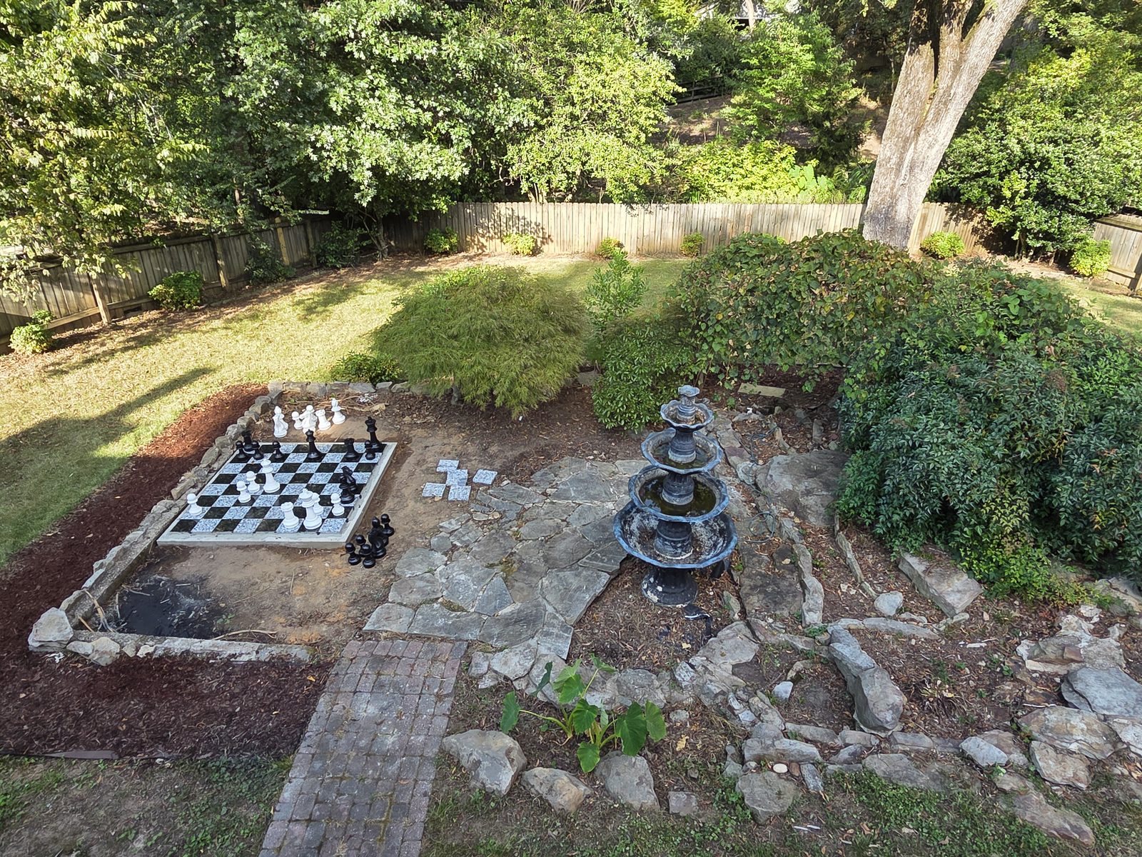Backyard with an outdoor chessboard, flagstone path, mulch beds, and a tiered fountain